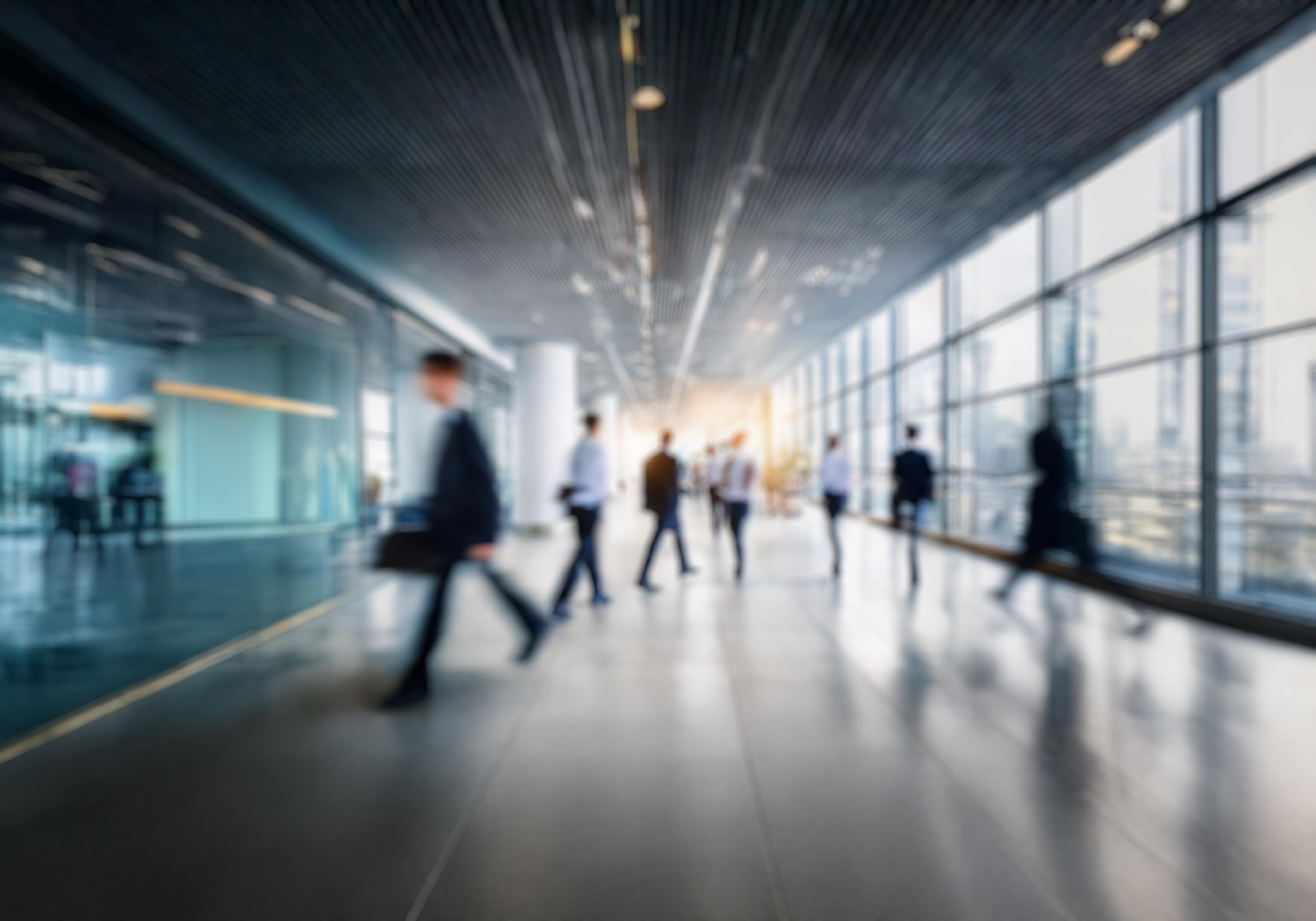 Blurred motion shot of business professionals walking through the corridor of a modern high-rise office building, representing the law firm and corporate environment Insight Economics serves.