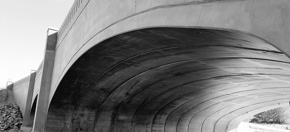 Black and white photograph of the underside of a concrete arch bridge or tunnel structure, showcasing Superior Ready Mix's commercial and infrastructure-grade concrete work in Southern California.